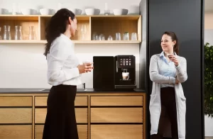 Two staff members using an automatic coffee machine in an office kitchen